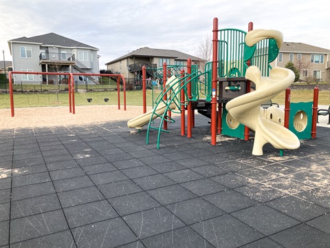 This multi level play structure features multiple climbing elements as well as two different slides. The area under the play structure has rubber tiles, adjacent to it, are belt and bucket swings on a sand surface.
