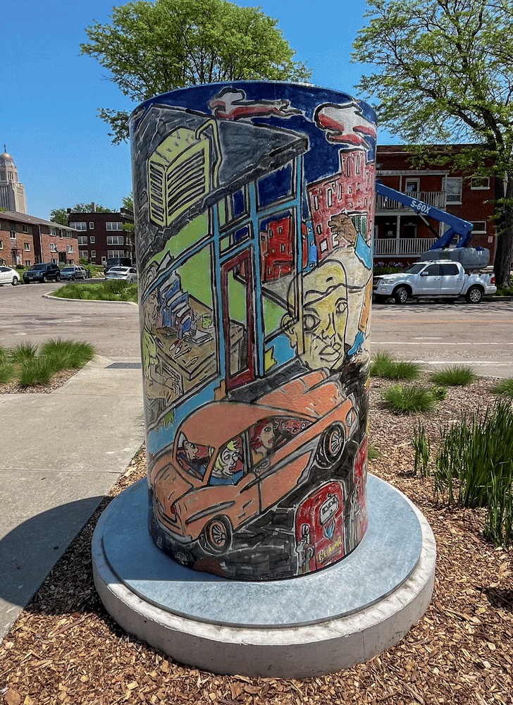 Rotating around the cylinder with a mural of a city scene with a gas station wrapping around it.