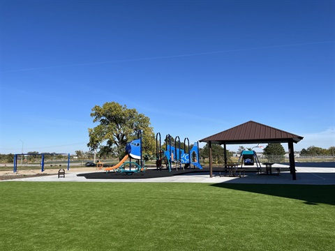 A playground in the near distance next to a small field of green grass and a shelter.