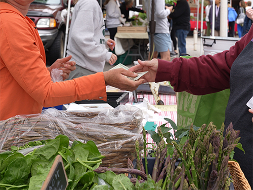 Photograph of people exchanging money at farmer's market